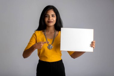 Gri bir arka planda elinde tabela tutan genç bir kız ya da iş kadını..