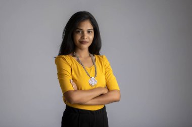 Gri arka planda elleri bağlı poz veren güzel, gülümseyen, duygusal bir genç kadının portresi..