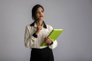 Güzel genç kız kitabı tutuyor ve gri arka planda poz veriyor.