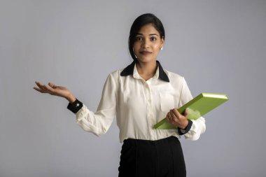 Güzel genç kız kitabı tutuyor ve gri arka planda poz veriyor.