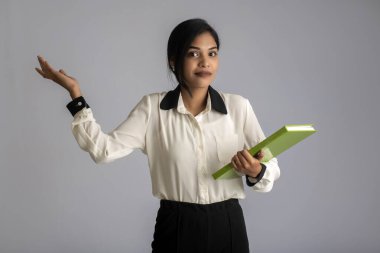 Güzel genç kız kitabı tutuyor ve gri arka planda poz veriyor.