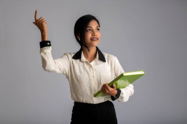 Güzel genç kız kitabı tutuyor ve gri arka planda poz veriyor.