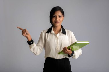 Güzel genç kız kitabı tutuyor ve gri arka planda poz veriyor.