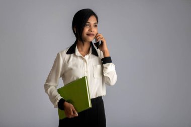 Güzel genç kız kitabı tutuyor ve gri arka planda cep telefonu kullanıyor.