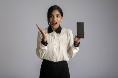 Gri arkaplanda boş ekran akıllı telefonu, cep telefonu ya da tablet telefonu tutan ve gösteren güzel bir kadın..