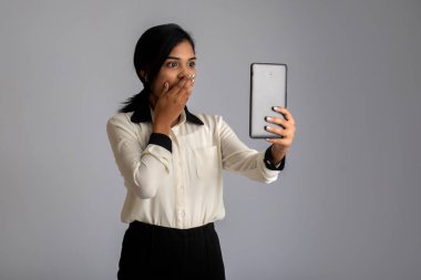 Gri arka planda cep telefonu ya da akıllı telefon kullanan genç bir Hintli kız.