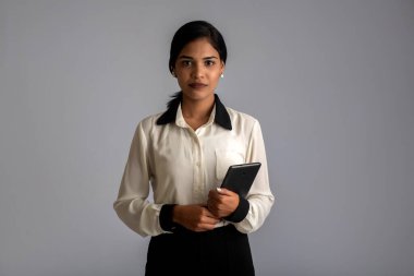 Gri arka planda cep telefonu ya da akıllı telefon kullanan genç bir Hintli kız.