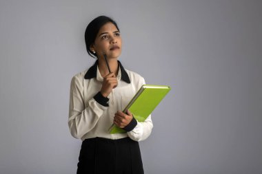 Gri arkaplanlı kitapla poz veren güzel genç kız.