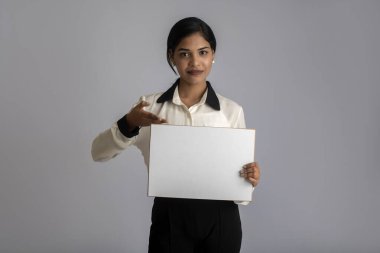 Gri bir arka planda elinde tabela tutan genç bir kadın ya da iş kadını..