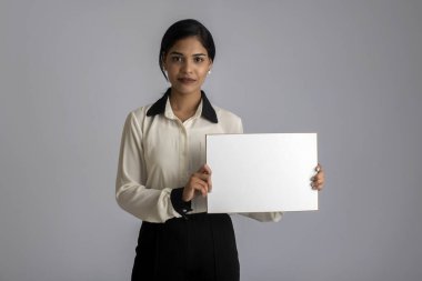 Gri bir arka planda elinde tabela tutan genç bir kadın ya da iş kadını..