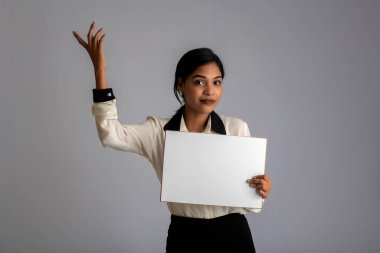 Gri bir arka planda elinde tabela tutan genç bir kadın ya da iş kadını..