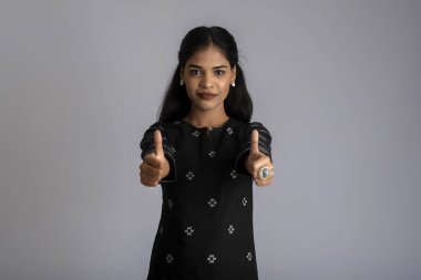 Gülümseyen genç kız gri bir arkaplanda işaret ya da baş parmak işareti gösteriyor