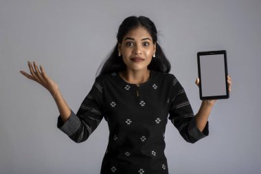 Gri arkaplanda akıllı telefon, cep telefonu ya da tablet telefonu tutan ve gösteren genç ve güzel bir kadın..