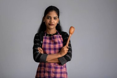 Gri arka planda mutfak aletleriyle poz veren genç bir kız.