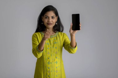 Gri arka planda cep telefonu ya da akıllı telefon kullanan genç kız