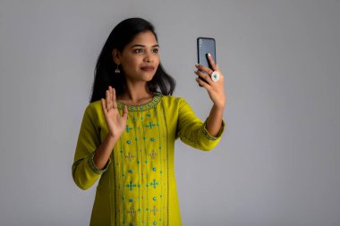 Gri arka planda cep telefonu ya da akıllı telefon kullanan genç kız