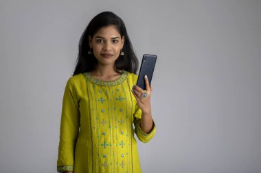 Gri arka planda cep telefonu ya da akıllı telefon kullanan genç kız