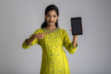 Gri arkaplanda akıllı telefon, cep telefonu ya da tablet telefonu tutan ve gösteren güzel bir kız..