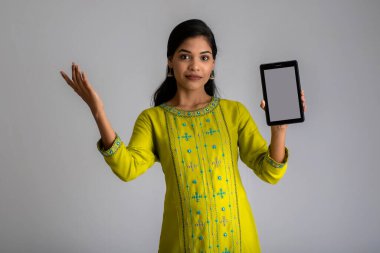 Gri arkaplanda akıllı telefon, cep telefonu ya da tablet telefonu tutan ve gösteren güzel bir kız..