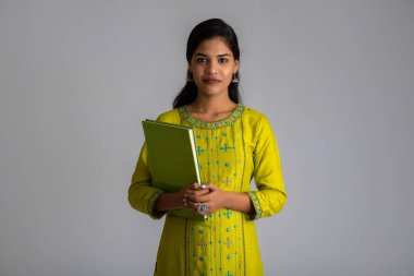 Gri arkaplanlı kitapla poz veren güzel genç kız.