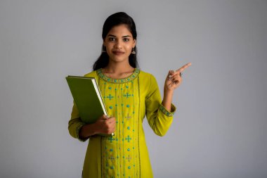 Gri arkaplanlı kitapla poz veren güzel genç kız.