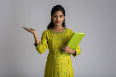 Gri arkaplanlı kitapla poz veren güzel genç kız.