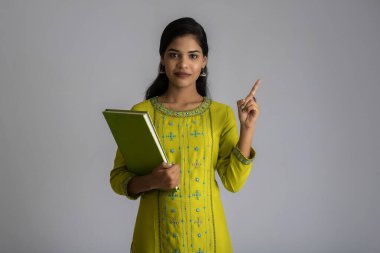 Gri arkaplanlı kitapla poz veren güzel genç kız.