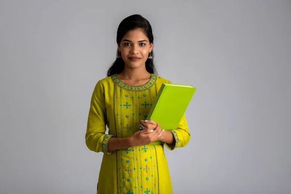 Gri arkaplanlı kitapla poz veren güzel genç kız.