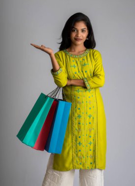 Gri bir arka planda alışveriş torbalarıyla poz veren güzel bir genç kız.