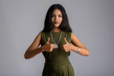 Gülümseyen genç kız gri bir arkaplanda işaret ya da baş parmak işareti gösteriyor