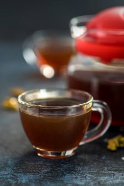 Bir fincan çay ve kakule kaşık şekerli ve dokulu arka planda.