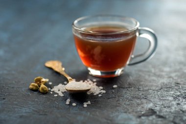 Bir fincan çay ve kakule kaşık şekerli ve dokulu arka planda.