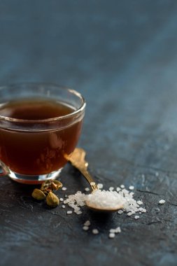 Bir fincan çay ve kakule kaşık şekerli ve dokulu arka planda.