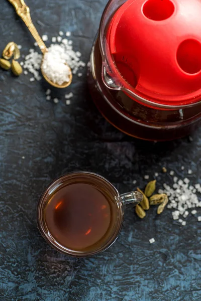 A cup of tea and cardamom with sugar in a spoon on a textured background.