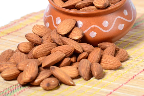 Almendras en una olla de barro con montón en estera de madera — Foto de Stock