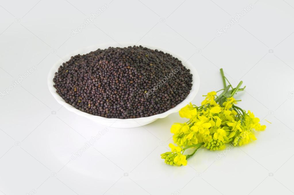 Heap of Brown Mustard seeds in bowl and mustard flower