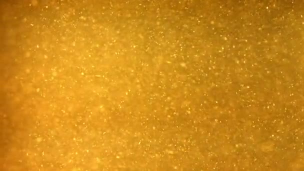 Particules brillantes qui s'écoulent dans un liquide jaune foncé 