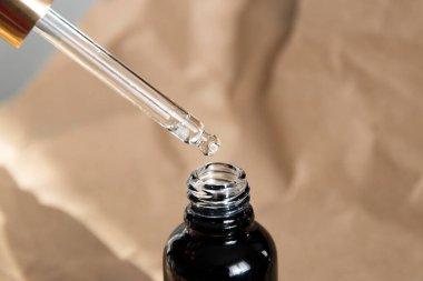 Aroma oil in glass black bottle on paper background. Oil jar mockup, concept of natural cosmetic. A drop of oil drips from a pipette.