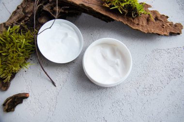 Vücut, yüz ve eller için ekolojik krem. Krema ve kozmetik için beyaz kavanoz. Kozmetik kutusu. Arka planda beton ve yosun dokusu var. Ağaçta yosun var. Modern kompozisyon. Krema kavanozu..