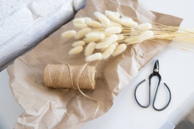 Beyaz lagurus ovatus çimleri kağıt üzerinde vintage makas ve rustik kenevir ipin yanında. Beyaz çiçekçi masası. Pamuk otu.