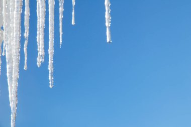 Mavi gökyüzüne karşı şeffaf buz saçakları. Kışın güneşte parlayan berrak buz. Donmuş su. Buz saçakları, su damlaları..
