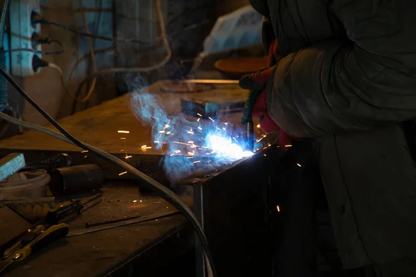 Worker welding metal and producing sparks. Man welding iron in his garage.