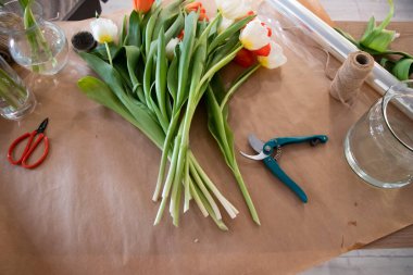 Çiçekçinin masası. Taze laleler ve mezhepçilerle dolu. Kırmızı ve beyaz laleler. Çiçekçi buket yapar. Bahar havası. 