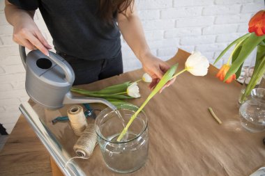 Çiçekçi vazoya taze çiçekli su döker. Bir çiçekçinin atölyesinde. El işi kağıtları masada. Laleli cam vazolar. Çiçeklerle çalışan kadın çiçekçi..