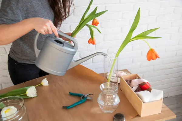 花屋は新鮮な花で花瓶に水を注ぎます 花屋の職場 テーブルの上のクラフト紙 チューリップ付きのガラス花瓶 花で働く女性花屋 — ストック写真