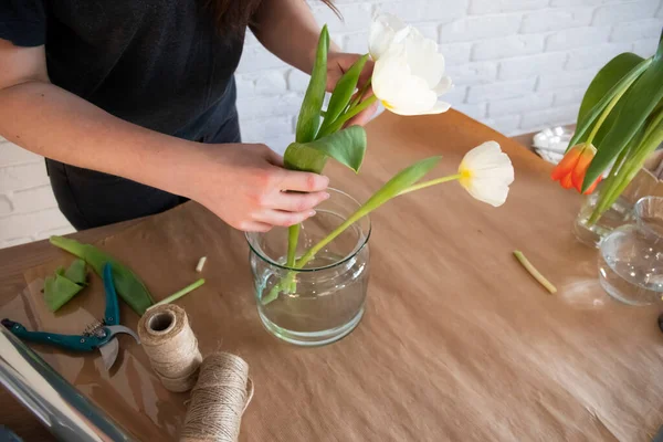 顧客のためのチューリップの創造的な花束の作成に取り組んでいる女性花屋 最上階だ 花屋で新鮮な白と赤のチューリップ 花屋さんの机にハサミと花瓶とセーター — ストック写真