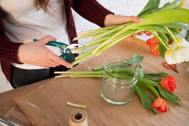 Çiçekçi, mezhepçilerle çiçekleri budar. Bir çiçekçinin atölyesinde. El işi kağıtları masada. Laleli cam vazolar. Çiçeklerle çalışan kadın çiçekçi..