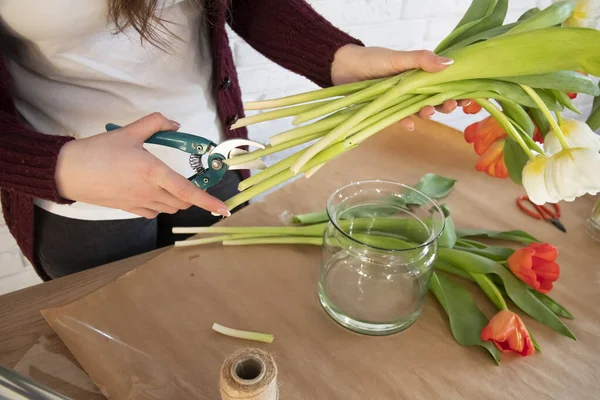 花はセーターで花を剪定します 花屋の職場 テーブルの上のクラフト紙 チューリップ付きのガラス花瓶 花で働く女性花屋 — ストック写真