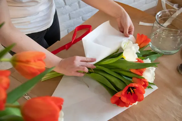 女性は白い紙に赤と白のチューリップの花束を梱包しています 花屋の職場だ 愛する人への贈り物を準備する 春の花のコンセプト — ストック写真