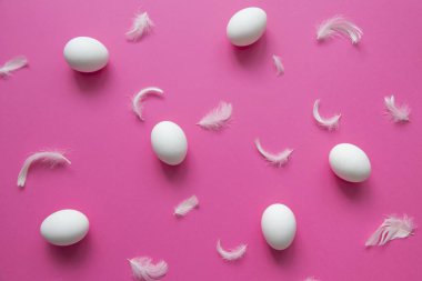 Modaya uygun yumurta deseni. Mutlu Paskalyalar. Pembe arka planda beyaz yumurta ve tüylerin düz görüntüsü. Minimalist stil. 